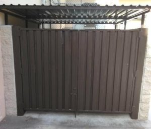 A neat black iron railing encloses a dumpster area along a concrete path, installed by Inland Empire Fencing to maintain a clean and orderly space.