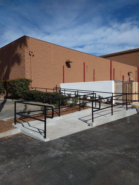 Commercial accessibility ramp with durable black railings, installed by Inland Empire Fencing, enhancing safety and mobility alongside an industrial building under a clear blue sky.