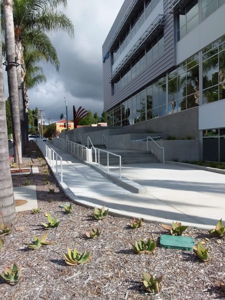 Modern commercial building with safety handrails and fencing by Inland Empire Fencing, featuring clear sky and palm trees in an urban setting, showcasing durable outdoor metal railings.