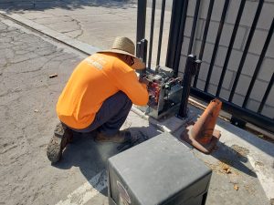 Technician from Inland Empire Fencing in orange safety shirt crouching to install an automated gate motor system, ensuring reliable and secure gate operation.