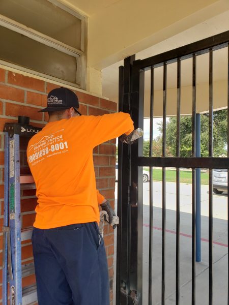 Fencing professional from Inland Empire Fencing using precision tools to install a durable metal gate, focusing on secure access control.
