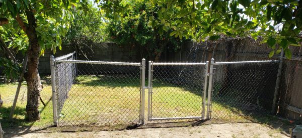 Residential chain-link gate set between trees, offering a secure yet inviting entry to a private backyard, part of Inland Empire Fencing's residential solutions.