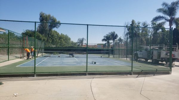 Chain-link fencing around a tennis court with workers in the background, installed by Inland Empire Fencing to provide a secure and unobtrusive boundary for sports areas.