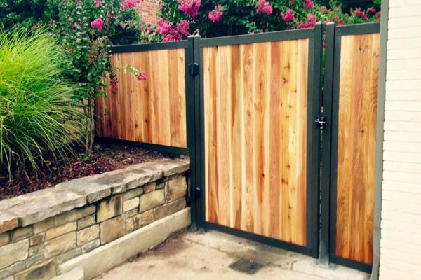 Custom-built wooden gate with metal reinforcement, enhancing privacy and curb appeal in a garden setting with vibrant flora.