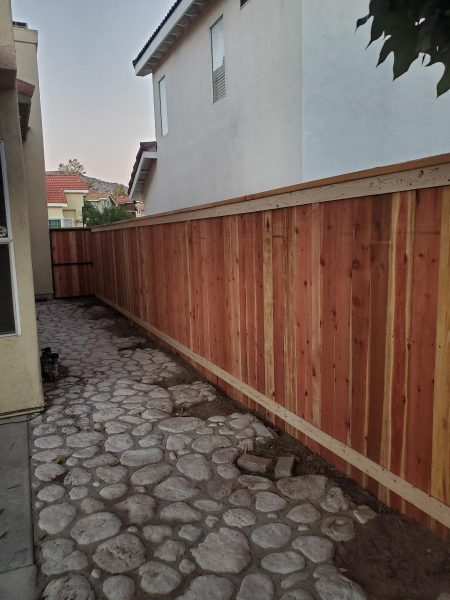 Privacy fence constructed with redwood panels alongside a cobblestone garden path, showcasing durable outdoor fencing.