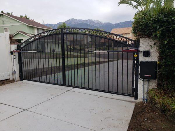 Residential driveway gate with arched design and decorative finials, featuring mesh for added security and transparency.