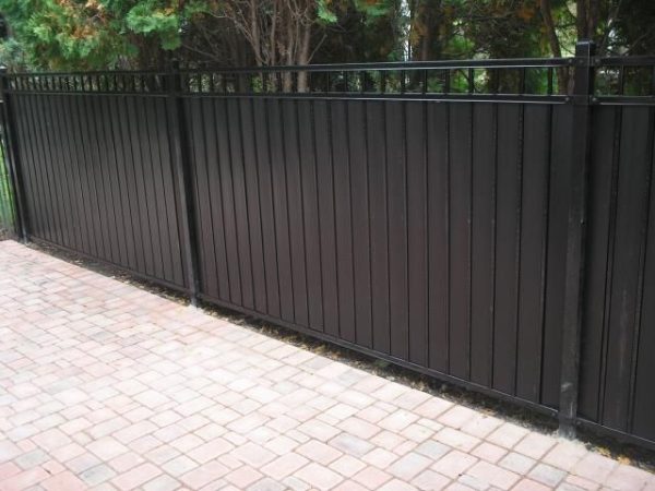 Black steel privacy fence with solid panels, offering a sleek and secure boundary for a paved residential area.